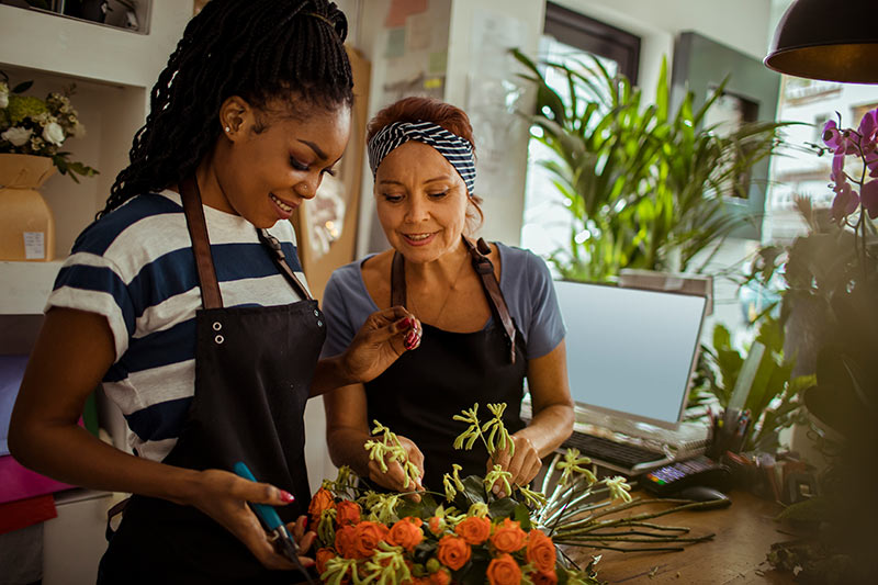 two female florists building a bouquet of orange flowers