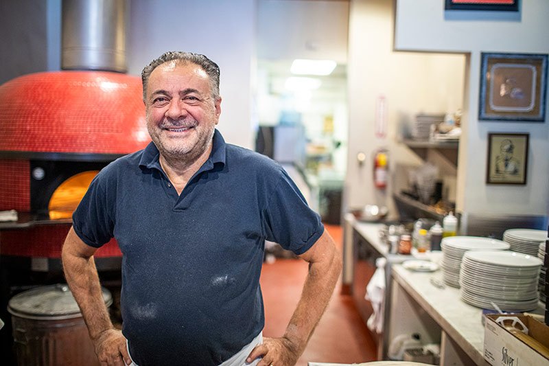 owner of an italian restaurant next to a pizza oven