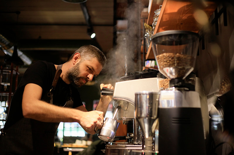 male barista steaming milk for a cafe latte