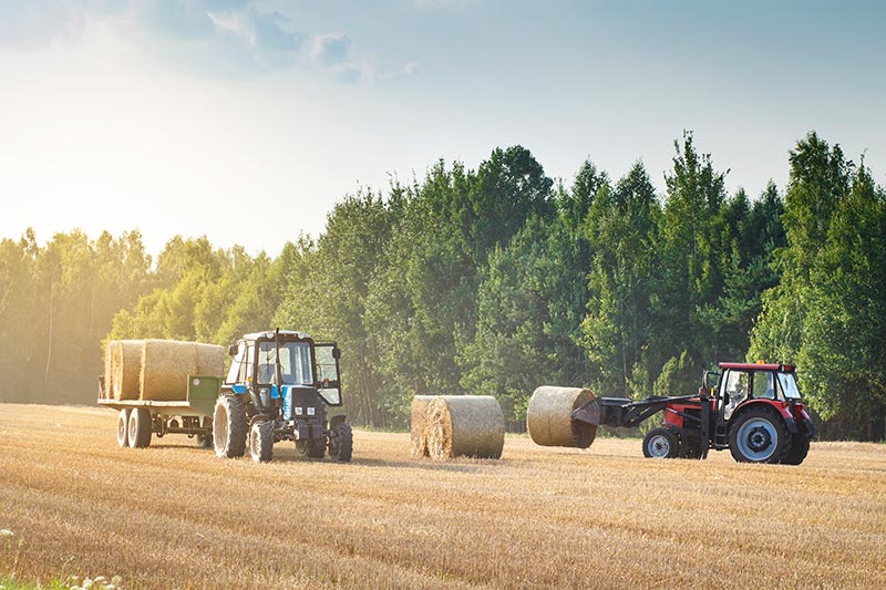farm tractors with tractor implements working in a hay field
