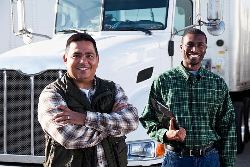 two truck drivers smiling next to a big rig